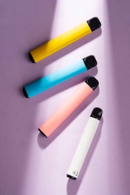Set of colorful disposable electronic cigarettes on a violet background with hard light. The concept of modern smoking. elf bar 