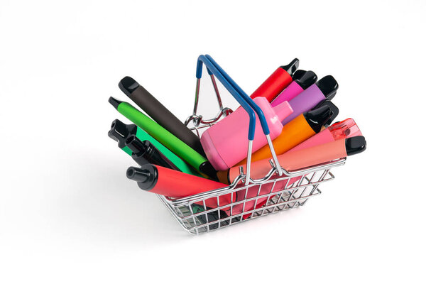 A set of colorful disposable electronic cigarettes of different shapes in a grocery basket on a white background with copy space. Concept of modern smoking.