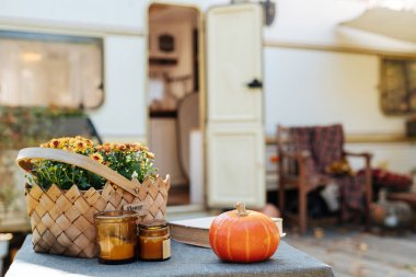 Mobile home decorated with Autumn decor. Festive atmosphere on wood table - pumpkin, flowers and book. Caravan camping. mobile home trailer.
