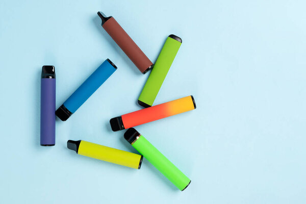 Layout of colorful disposable electronic cigarettes with shadows on a blue background. The concept of modern smoking, vaping and nicotine. Top view.
