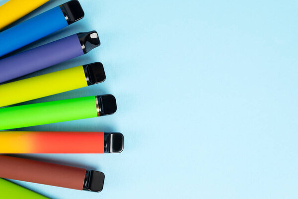 Layout of colorful disposable electronic cigarettes with shadows on a blue background. The concept of modern smoking, vaping and nicotine. Top view.