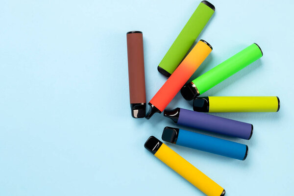 Layout of colorful disposable electronic cigarettes with shadows on a blue background. The concept of modern smoking, vaping and nicotine. Top view.