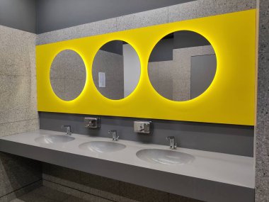 Modern banyo içi taştan gri fayanslar, lavabo ve yuvarlak sarı aynalarla dolu. Lavabosu ve musluğu olan banyo. Havaalanında ya da restoranda umumi tuvalet, kafe, ofis.