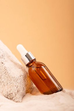 Cam şişe nemlendirici yüz serumu, kumlu zeminde kozmetik yağ. Yaz yüz bakımı konsepti