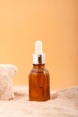 Cam şişe nemlendirici yüz serumu, kumlu zeminde kozmetik yağ. Yaz yüz bakımı konsepti