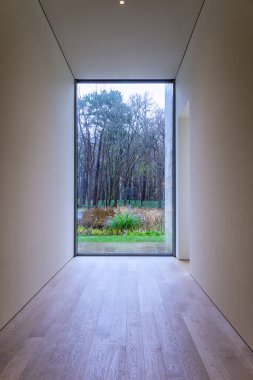 Işık duvarında siyah çerçeveli koridor penceresi ve yeşil bitkilerin arka plan manzarası içeriden ön manzara.