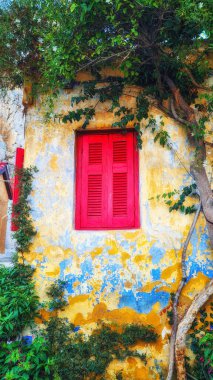 Atina 'nın Anafiotika kentinde solmuş bir duvar üzerindeki kırmızı ahşap panjurlu eski kır evi penceresi.