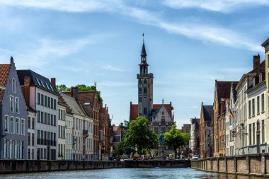 Kanaldaki tekneden Jan Van Eyck Meydanı 'nın görüntüsü. Mavi gökyüzü ve biraz bulut. Merkezdeki fakir yamaç yüksek bir kule ve Bruges 'ün tipik mimarisidir..