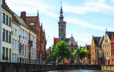 Kanaldaki tekneden Jan Van Eyck Meydanı 'nın görüntüsü. Mavi gökyüzü ve biraz bulut. Merkezdeki fakir yamaç yüksek bir kule ve Bruges 'ün tipik mimarisidir..