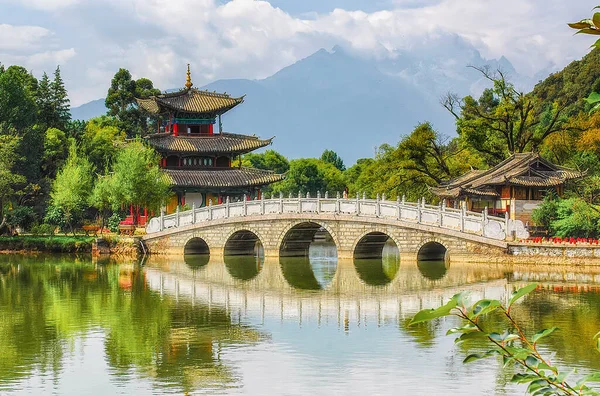 Scenic view of the Suocui Bridge over the Black Dragon Pool and the Moon Embracing Pavilion in the Jade Spring Park, Lijiang, China. The Jade Dragon Snow Mountain is visible in background.