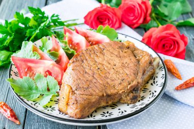 Fırında fırında domuz filetosu, yanında da domates ve bitki.