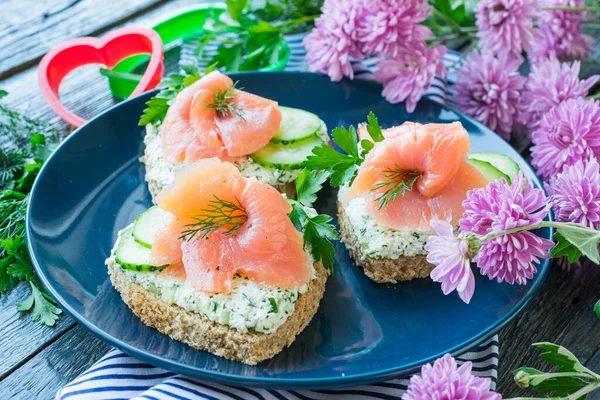 Sandwiches with salmon, cottage cheese and cucumber in the form of a heart on a blue ceramic plate