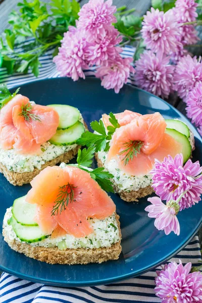 Sandwiches with salmon, cottage cheese and cucumber in the form of a heart on a blue ceramic plate