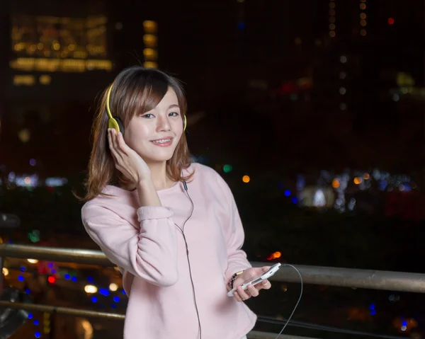 Vacker asiatisk kvinna bär hörlurar och hålla mobiltelefon — Stockfoto