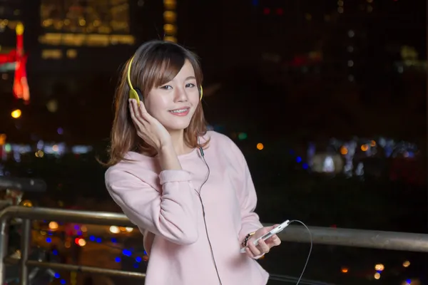 Hermosa mujer asiática usando auriculares y sosteniendo el teléfono celular — Foto de Stock