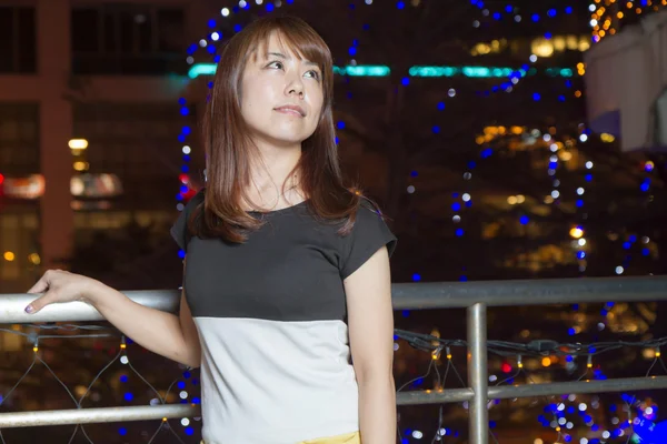 Mujer asiática sonriente frente a las luces de la ciudad — Foto de Stock