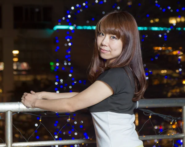 Mujer asiática sonriente frente a las luces de la ciudad — Foto de Stock