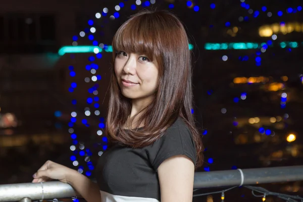 Mujer asiática sonriente frente a las luces de la ciudad — Foto de Stock