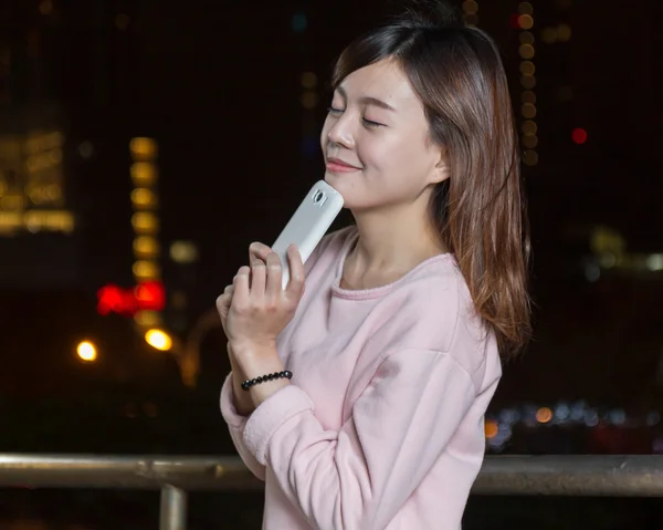 Atraente asiático mulher segurando celular por luzes brilhantes — Fotografia de Stock