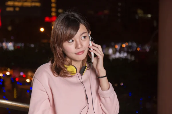 Schöne asiatische Frau spricht auf Smartphone und gelbem Kopfhörer — Stockfoto