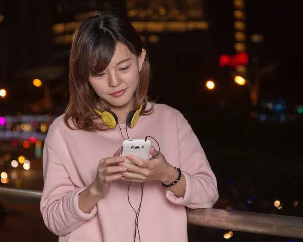 Mulher asiática bonita com telefone inteligente e fones de ouvido amarelos — Fotografia de Stock