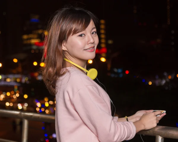 ผู้หญิงเอเชียสวยที่มีสมาร์ทโฟนและหูฟังสีเหลือง — ภาพถ่ายสต็อก