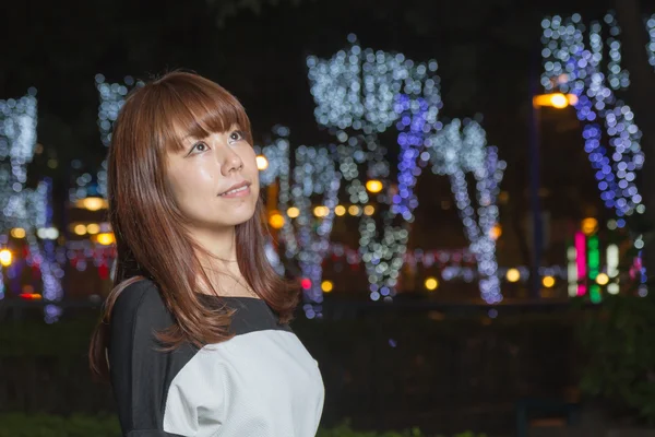 Asiatico donna standing in un parco con luci dietro di lei — Foto Stock