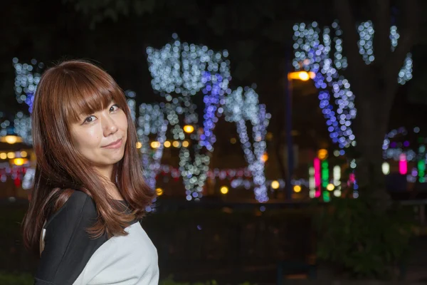 Asiatisk kvinna som står i en park med belysning bakom henne — Stockfoto