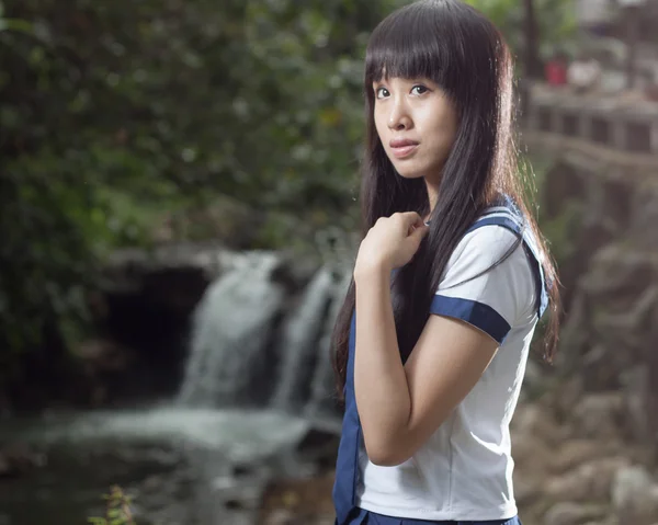 Asiatische Schulmädchen steht vor Wasserfall — Stockfoto