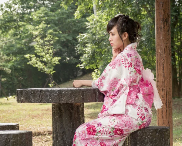 Asijské žena nosí kimono u stolu v japonské zahradě — Stock fotografie