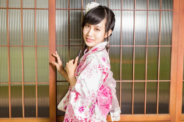 Mujer asiática usando un kimono frente a ventanas de madera japonesas — Foto de Stock