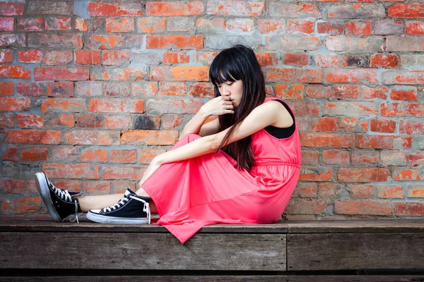 年轻的亚裔女子坐在红砖砌成墙非常沮丧和悲伤 — 图库照片