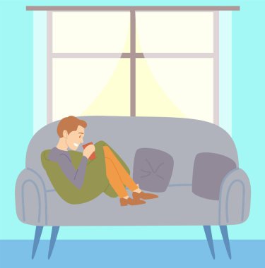 Kanepede oturan bir adam evde çay ya da kahve içiyor. İnsan evde yalnız vakit geçirir.