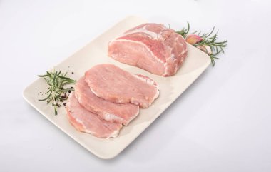 Raw pork loin in chops and in cross-section with spices, herbs on a white plate, on white background. Packshot photo.