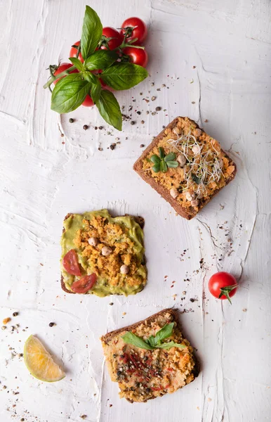 Sandwiches with vegetable pate and fresh veggies, top view. Plant based, meat free products. Vegan, vegetarian concept. Vertical composition with sandwiches on white vintage background.