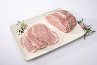 Çiğ domuz eti, fileto, beyaz tabakta jambon, beyaz arka plan, üst manzara. Pirzola ve enine kesitte taze çiğ et, baharatlar ve taze otlarla dolu bir tabakta. Bir sürü fotoğrafı..