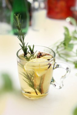 Biberiyeli bitki çayı, karanfil, zencefil, bal ve limon berrak cam bir fincanda, kupa, beyaz, bulanık arka planda. Ferahlatıcı ve sağlıklı bitkisel içecek, aşılama, dikey görüş.
