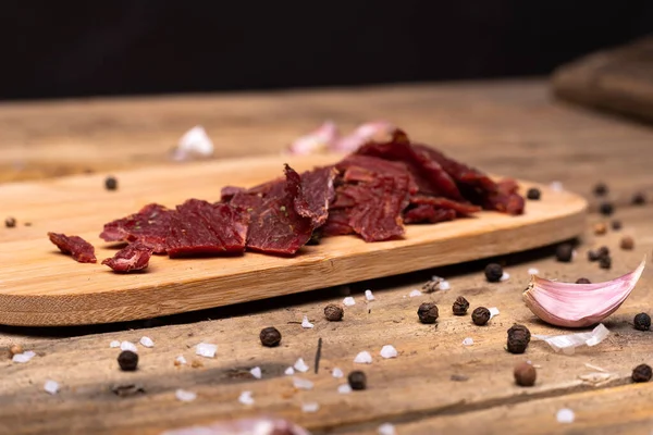 Skład rustykalny z przyprawami, suszony czosnek i wołowina, suszone kawałki mięsa wołowego na desce do krojenia drewna, widok poziomy. — Zdjęcie stockowe