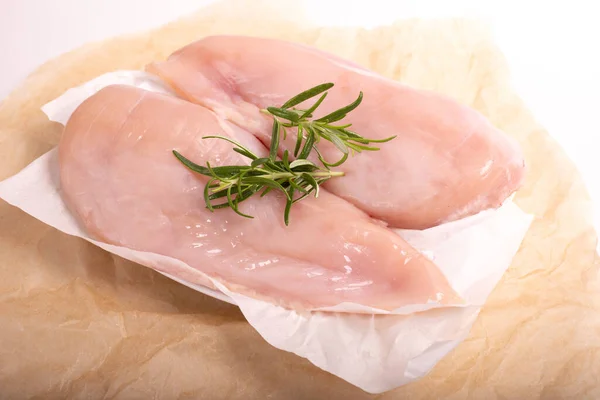 Raw chicken breast, fillet, on a kraft food paper. Poultry raw meat decorated with rosemary sprigs.