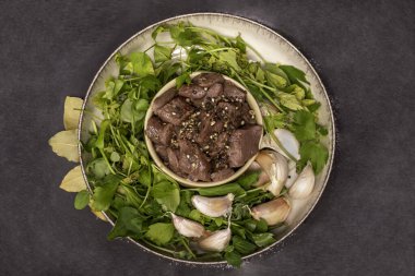 Çiğ oyun, küp halinde sığır eti ve tabakta taze otlar, siyah arka planda, üst manzara. Parçalanmış kırmızı etle kompozisyon.