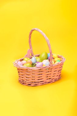 Sarı arka planda renkli Paskalya yumurtalarıyla dolu bir Paskalya sepeti. Paskalya tatili konsepti, fotokopi alanı olan fotoğraf.