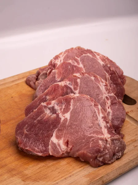 Domuz eti pirzolaya, dilimlere, tahta kesme tahtasına, beyaza kesilmiş. Çiğ domuz boyunlu biftek, pirzola, yakın plan.. — Stok fotoğraf
