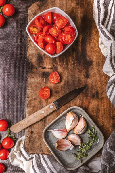 Склад з вишневими помідорами, часником, свіжими травами та ножем на вінтажній дошці для різання деревини, вид зверху . — стокове фото