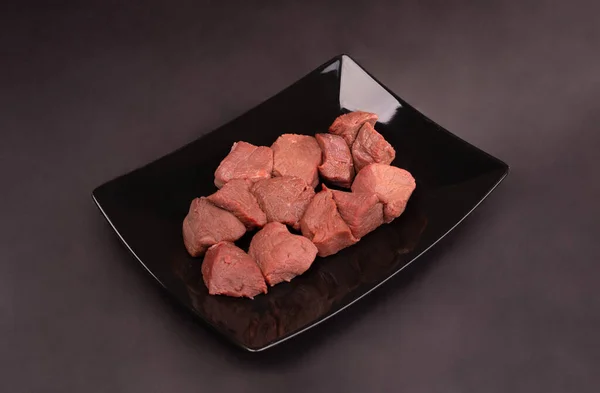 Surowe mięso, wołowina na czarnym talerzu. Czerwone mięso w kostkach, na czarnym tle, tablica. — Zdjęcie stockowe