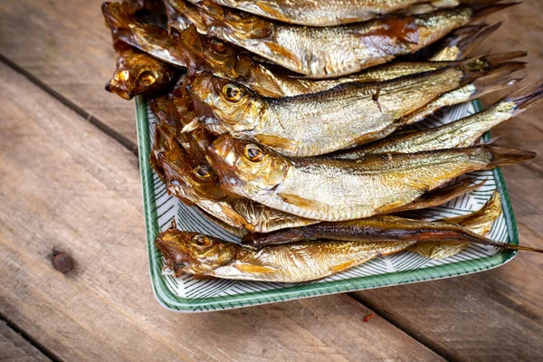 Ahşap bir arka planda serpilmiş. Küçük füme balık, tabakta atıştırmalıklar, eski moda ahşap tahta üzerinde..
