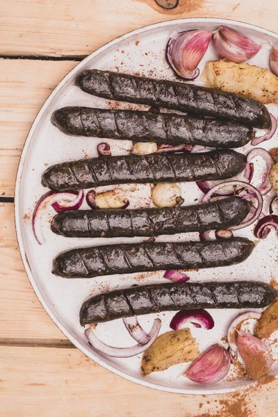 Grilled, roasted vegan, vegetarian sausages. Rustic composition with meat free products, buckwheat blood sausages, onion, garlic and spices, on a plate, on a wooden background, top view.
