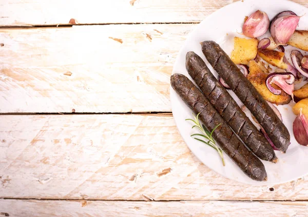 Grilled, roasted vegan sausages. Rustic composition with meat free products, buckwheat blood sausages, onion, garlic and spices, on a plate, on a wooden background, top view, with a copyspace.
