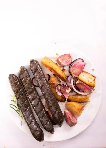 Grilled, roasted vegan sausages on a plate, selective focus. Composition with meat free products, buckwheat blood sausages, potatoes, onion, garlic and spices, on a white background, isolated.