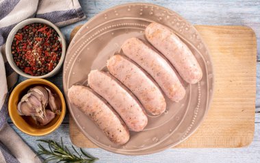 Geleneksel Polonya buharda pişirilmiş beyaz sosisi bir tabakta, bir kesme tahtasının üzerinde, ahşap bir zeminde. Beyaz haşlanmış sosis, baharat ve taze sarımsaklı Rustik kompozisyon. Paskalya lezzeti, üst görünüm.