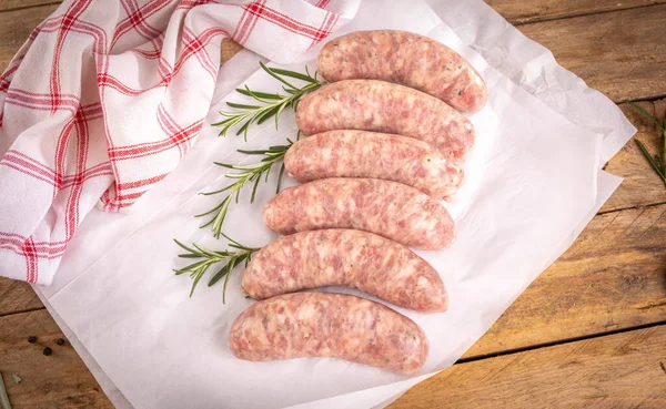 Rustic composition with white sausage and fresh rosemary. Easter delicacy. Traditional raw white sausage on a white paper, on a cutting board, on a wooden background.